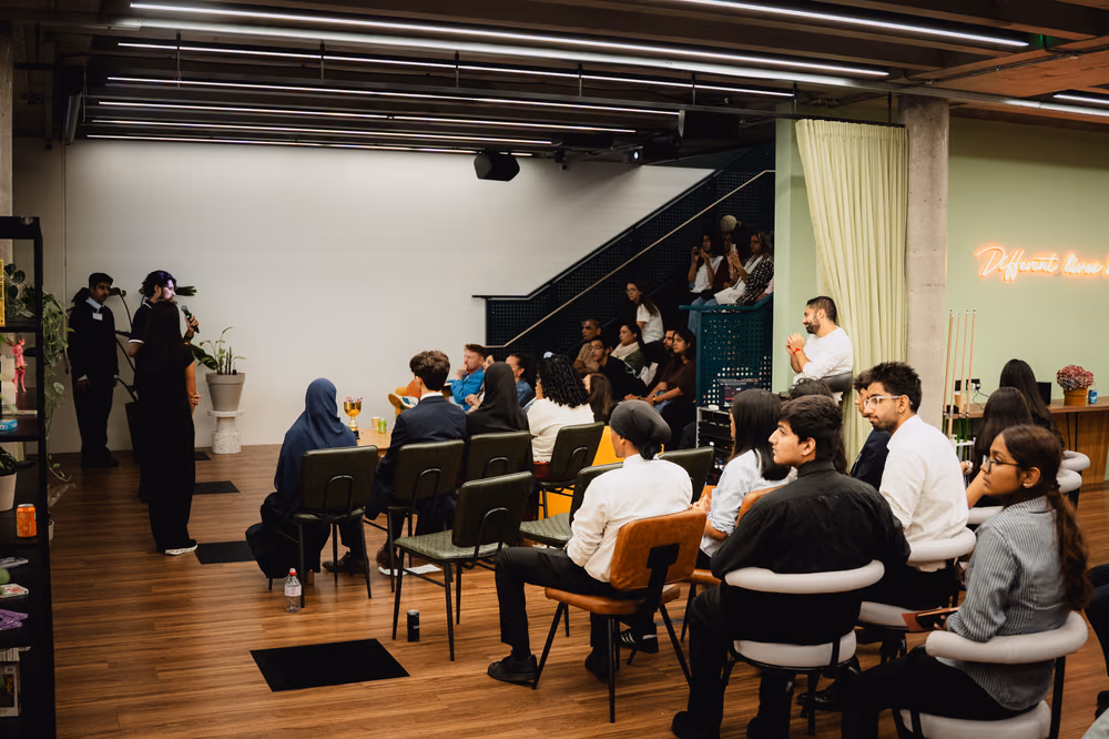 The audience seated across the room while a team pitches.